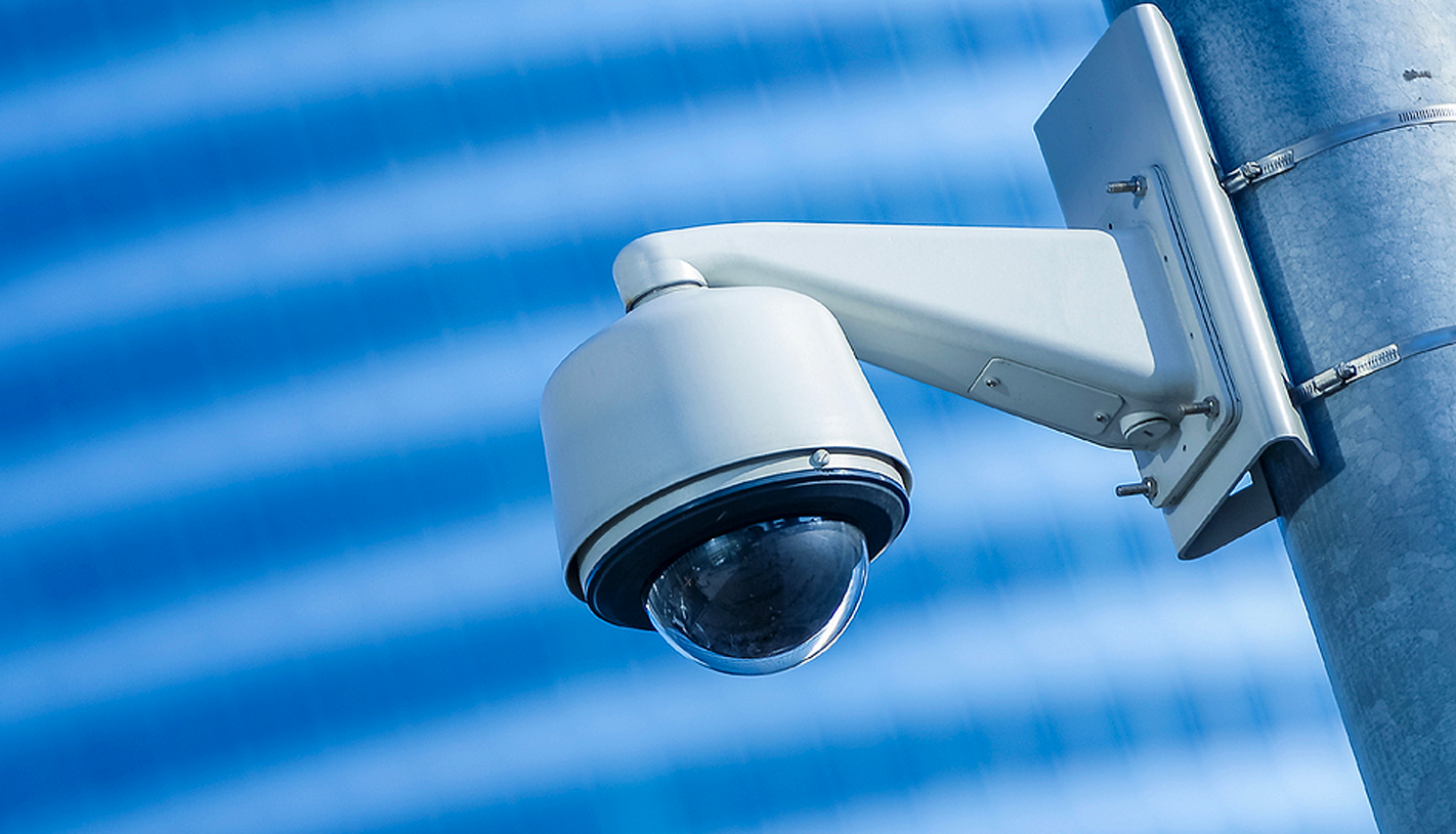 A security camera mounted to a pole against a blue patterned background